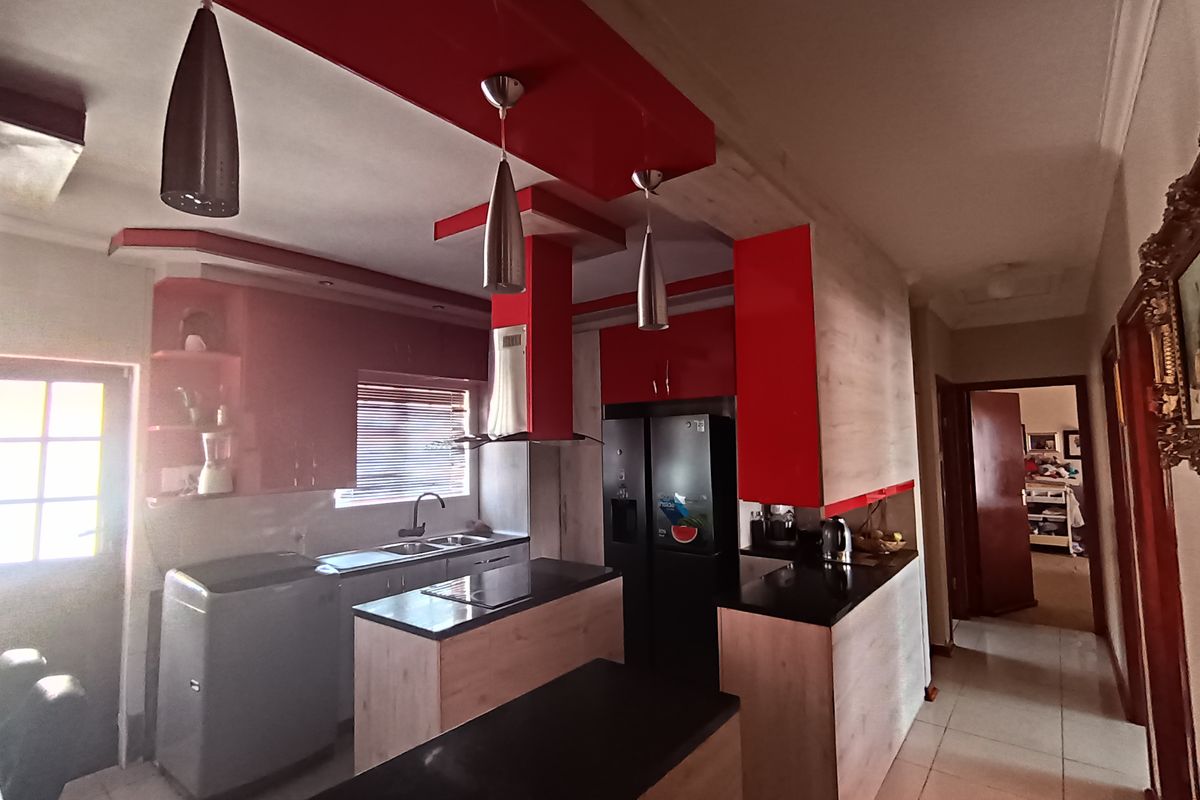 Modern kitchen featuring bold red cabinetry, a central island with a dark countertop, integrated extractor fan, and tiled flooring.