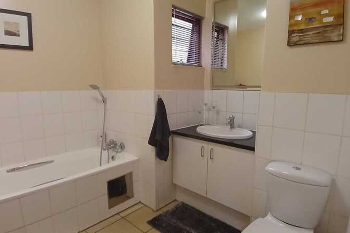 A functional bathroom featuring a built-in bathtub with shower mixer, a vanity with basin, and a standard toilet.