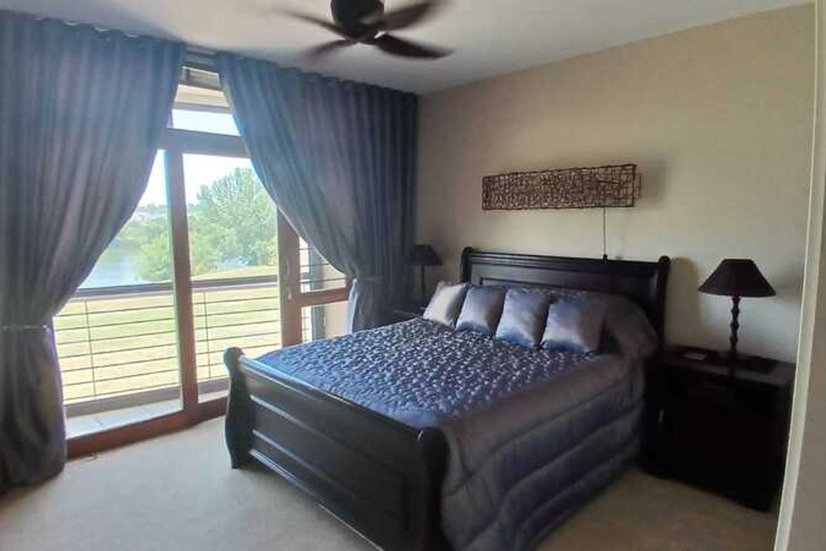 A well-maintained bedroom featuring large sliding glass doors that open to a balcony with scenic water views and a ceiling fan.