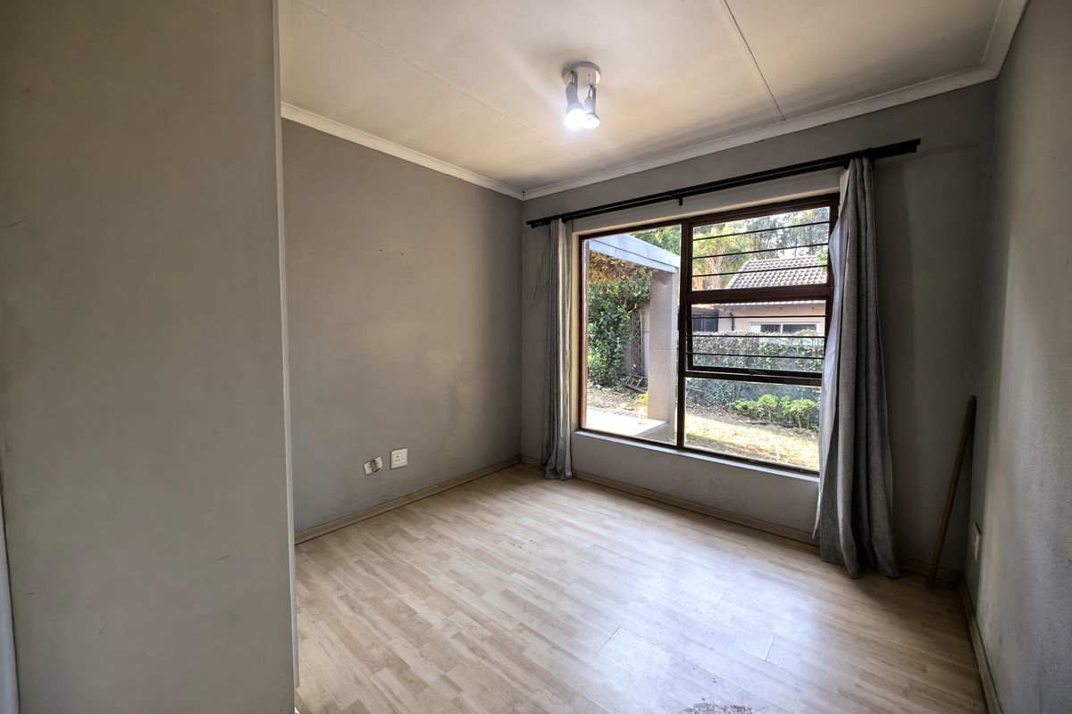 A vacant bedroom featuring light wood-look laminate flooring, neutral grey walls, and a large window overlooking the rear garden area.
