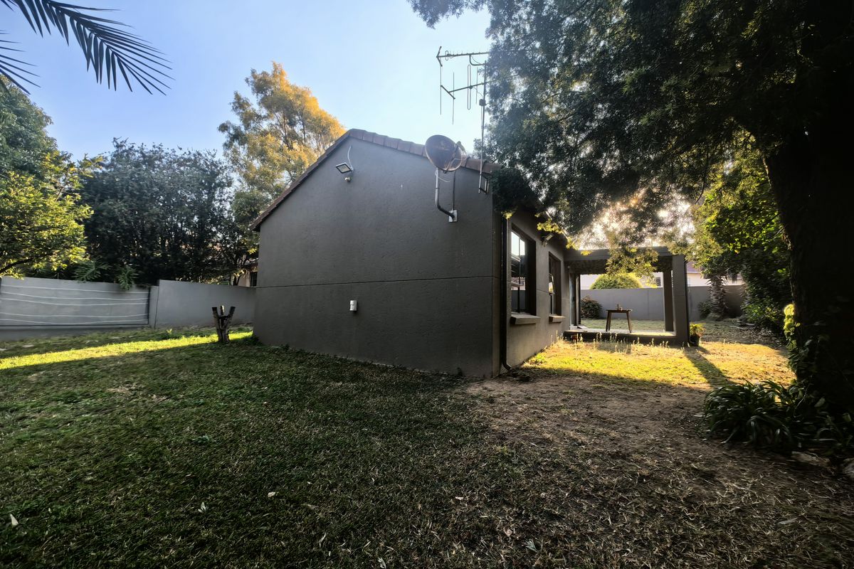 A view of the rear exterior of the cluster home, featuring a private garden, paved patio area, and mature trees.