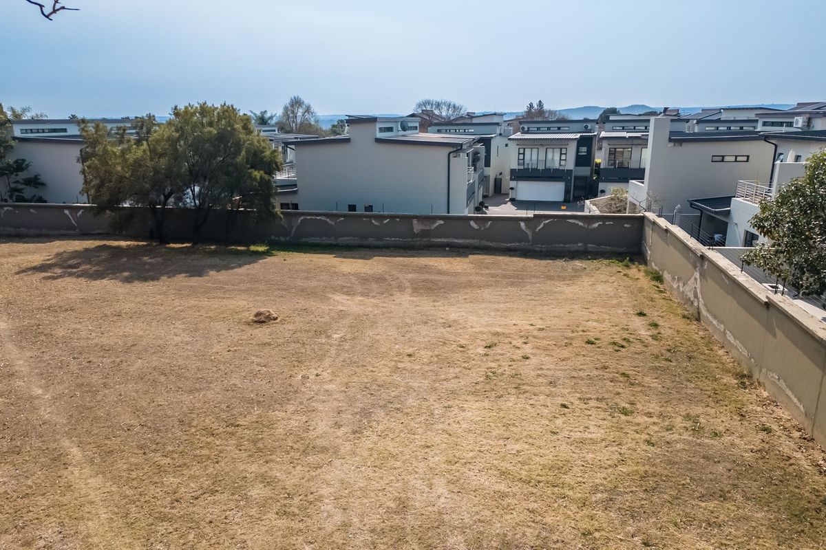 A vacant residential plot featuring a perimeter boundary wall, situated within an established residential estate.