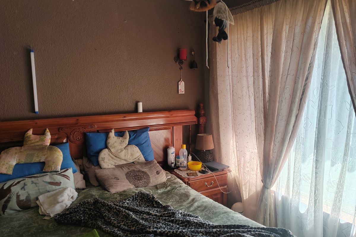 A bedroom featuring a wooden headboard, wall-mounted light fixture, and large window with curtains allowing natural light.