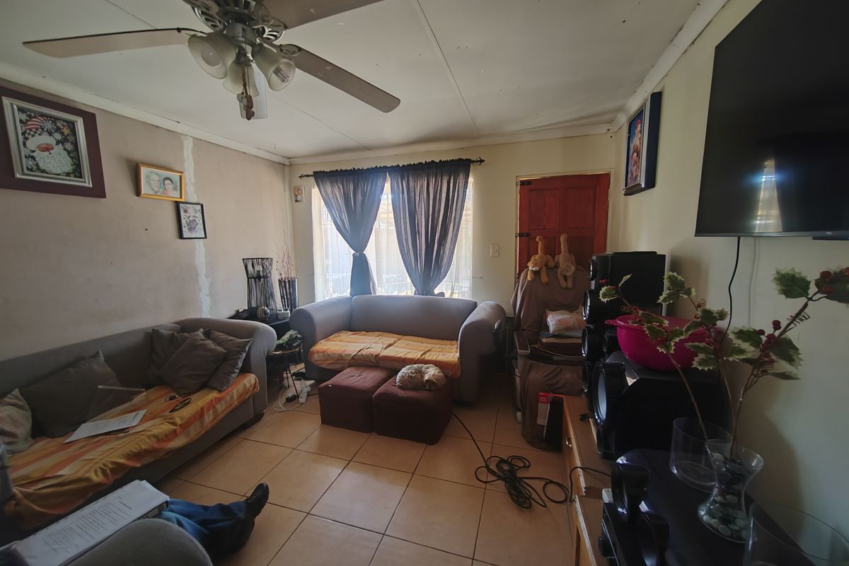 A living room featuring tiled flooring and a ceiling fan, with visible wall surface wear requiring maintenance.