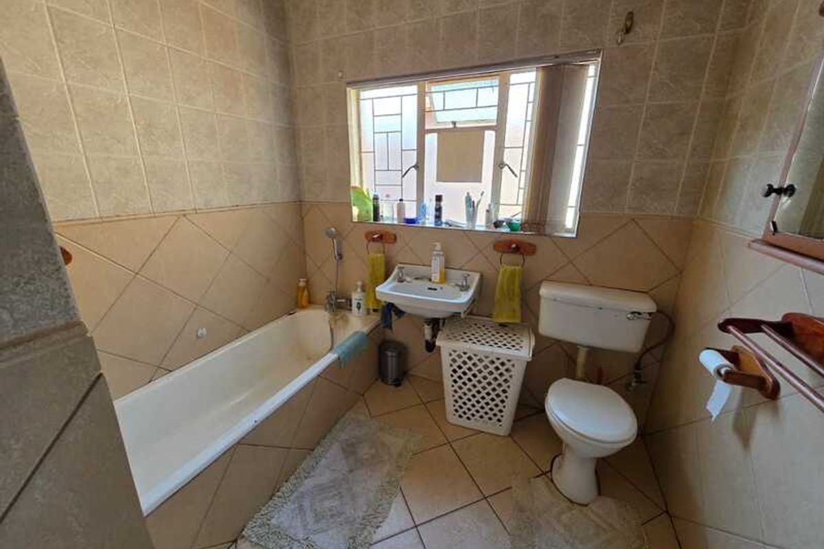 A dated bathroom featuring a standard bathtub, wall-mounted basin, and toilet with full-height wall tiling and tiled flooring.