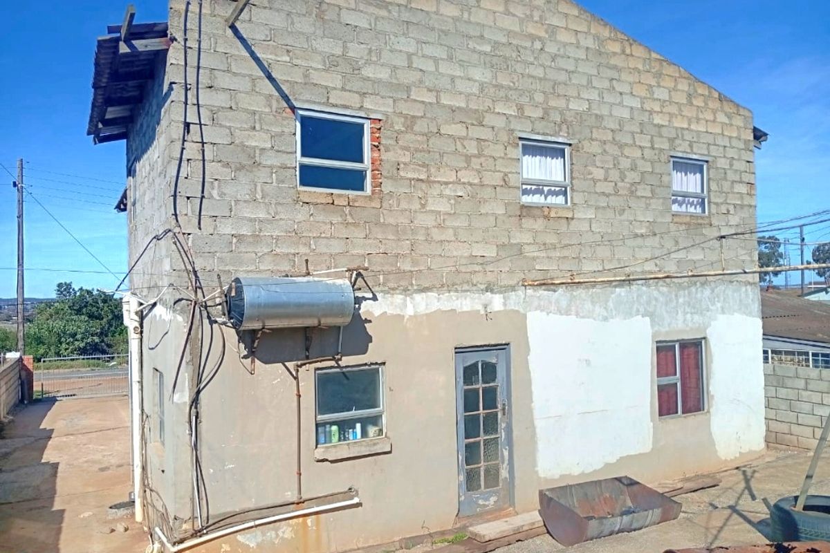 Rear elevation of a two-story residential structure featuring exposed concrete blockwork, an external solar water heater, and unfinished exterior wall finishes.