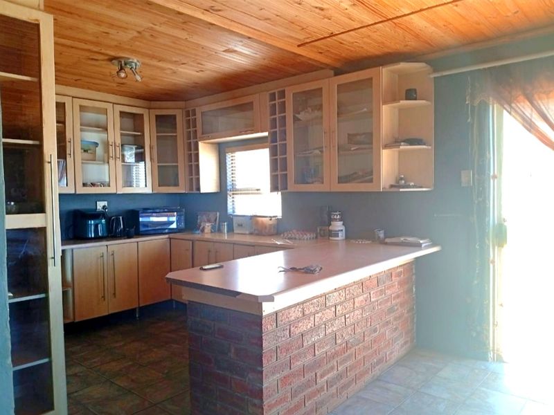 A kitchen featuring timber ceilings, built-in cabinetry with glass-fronted doors, and a brick-faced breakfast bar with tiled flooring.