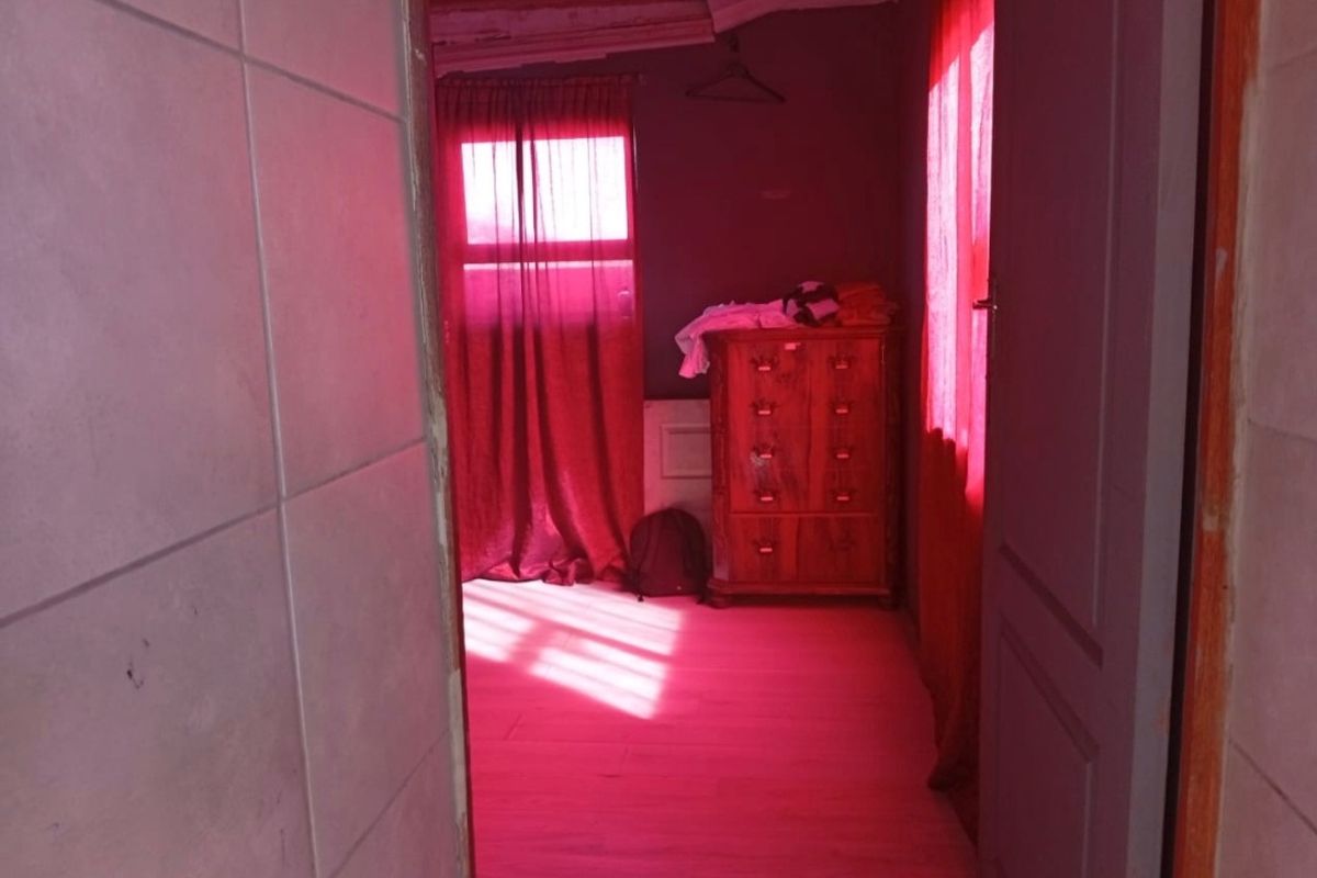 A bedroom interior featuring laminate flooring and tiled wall sections, currently requiring cosmetic updates and improved lighting to enhance the space.