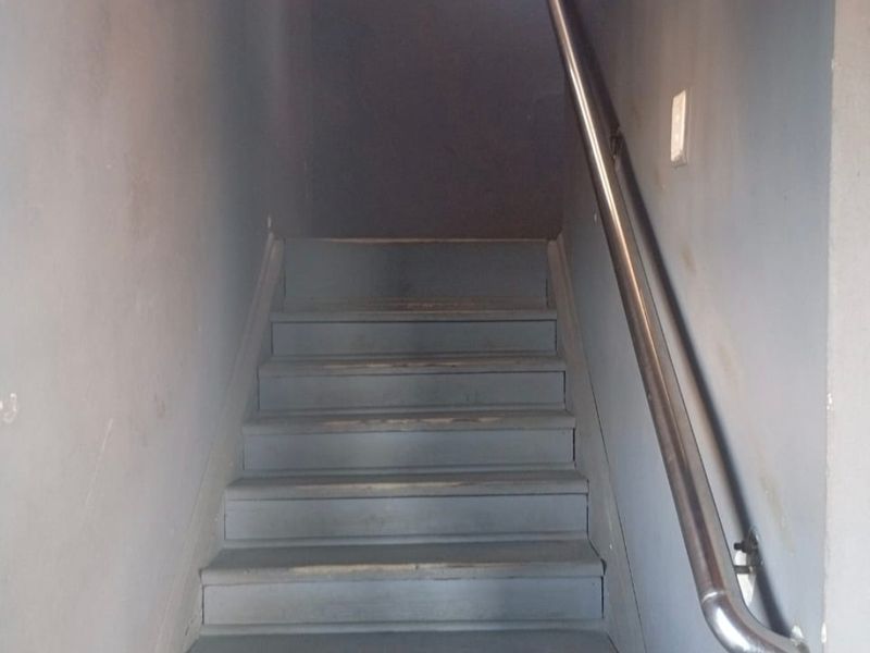 A narrow interior staircase featuring a metal handrail and painted wooden steps showing signs of wear.