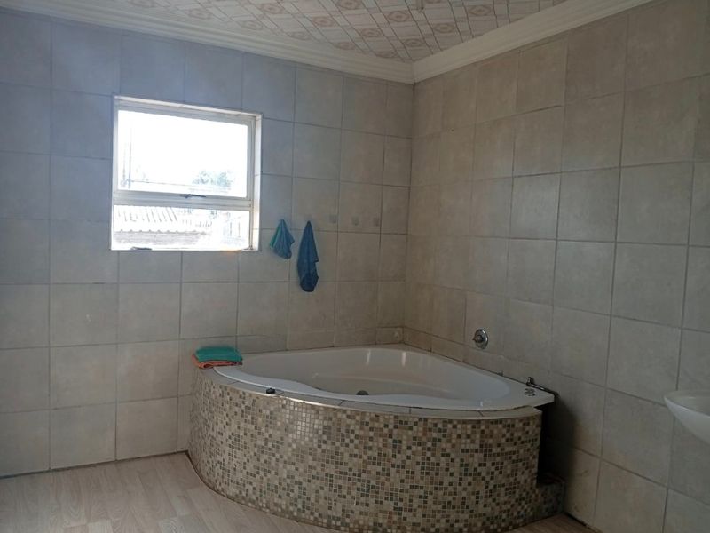 A bathroom featuring a corner bathtub with a mosaic tile surround, full wall tiling, and a basin, requiring cosmetic updates to improve the finish.