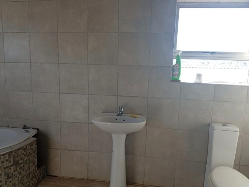 A functional bathroom featuring a pedestal basin, built-in bathtub with mosaic detailing, and neutral wall tiling.