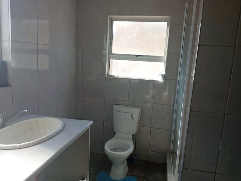 A functional bathroom featuring a vanity basin, toilet, and shower enclosure with neutral wall and floor tiling.