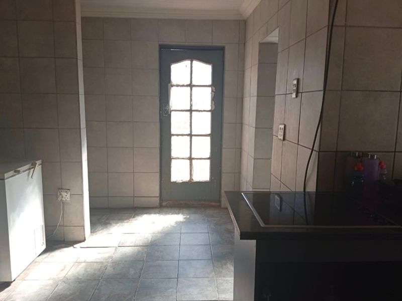 A functional kitchen space featuring fully tiled walls and floors, a built-in hob, and a glass-paneled exterior door.