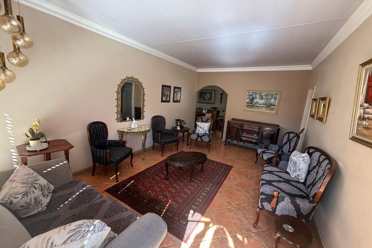 A spacious living room featuring terracotta floor tiles, crown molding, and a classic arched doorway leading to an adjacent area.