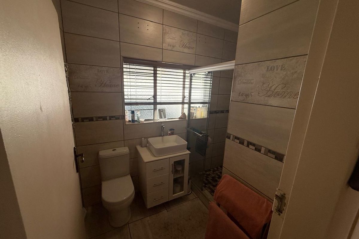A compact bathroom featuring a vessel sink vanity, a toilet, and a glass-enclosed shower with decorative wall tiling.