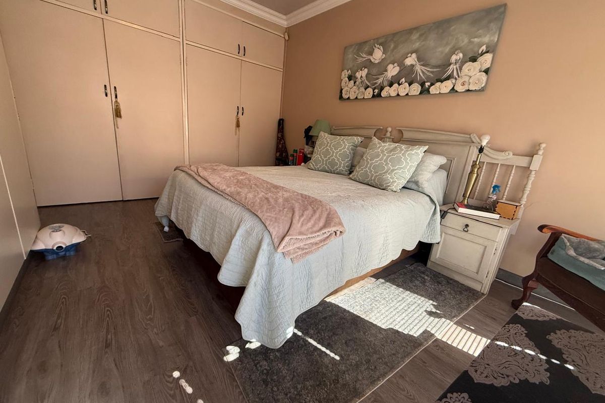 A bedroom featuring wood-look laminate flooring, built-in floor-to-ceiling wardrobes, and neutral wall tones.