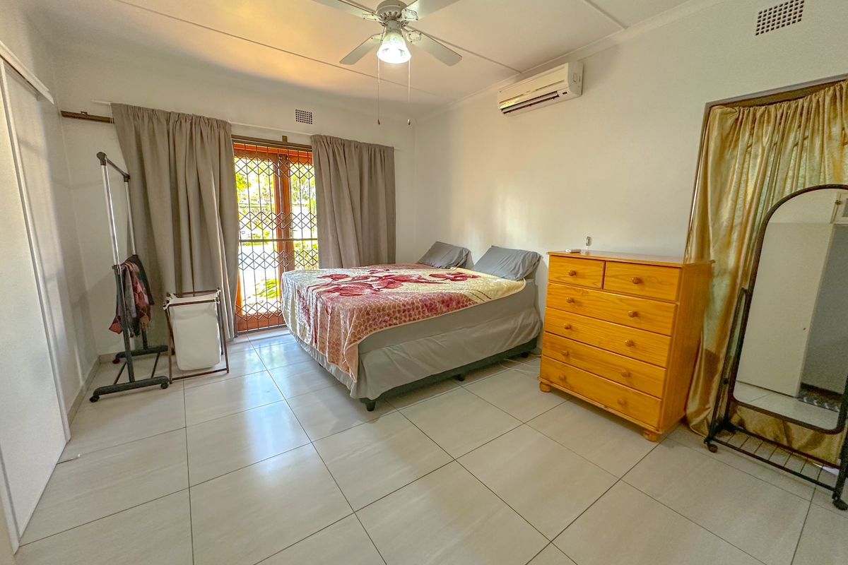 A spacious bedroom featuring large floor tiles, a ceiling fan, and a wall-mounted air conditioning unit, with direct access to the exterior.