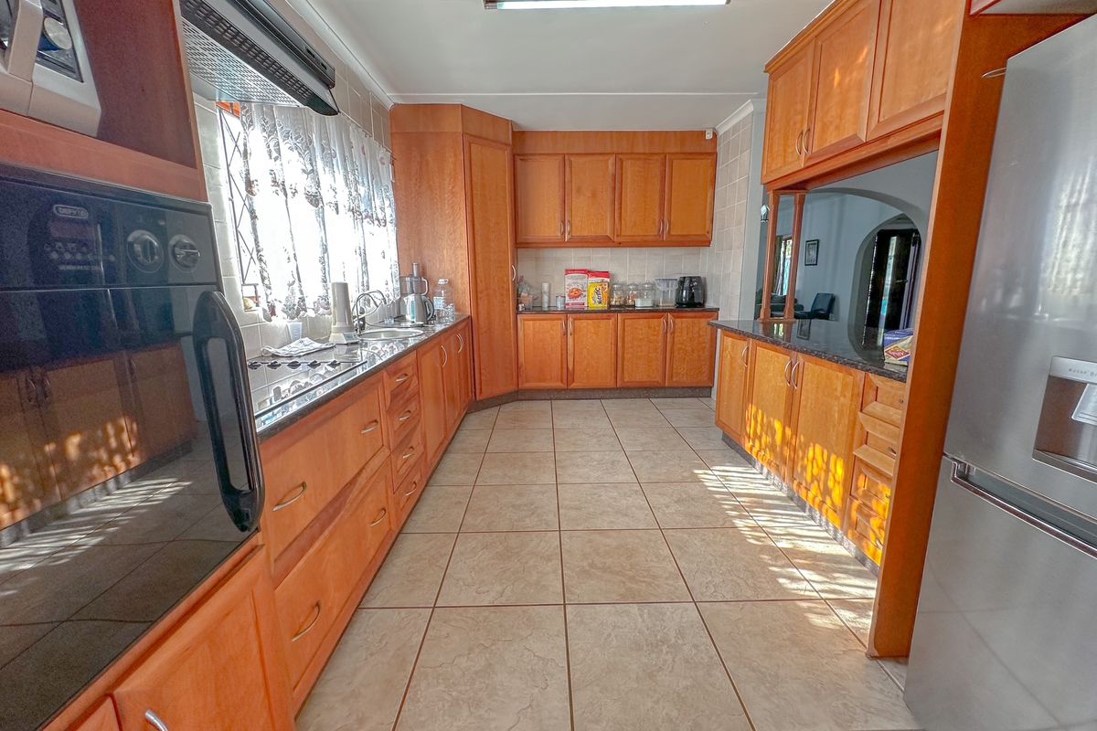 A functional kitchen featuring wooden cabinetry, granite countertops, tiled flooring, and built-in oven and hob appliances.