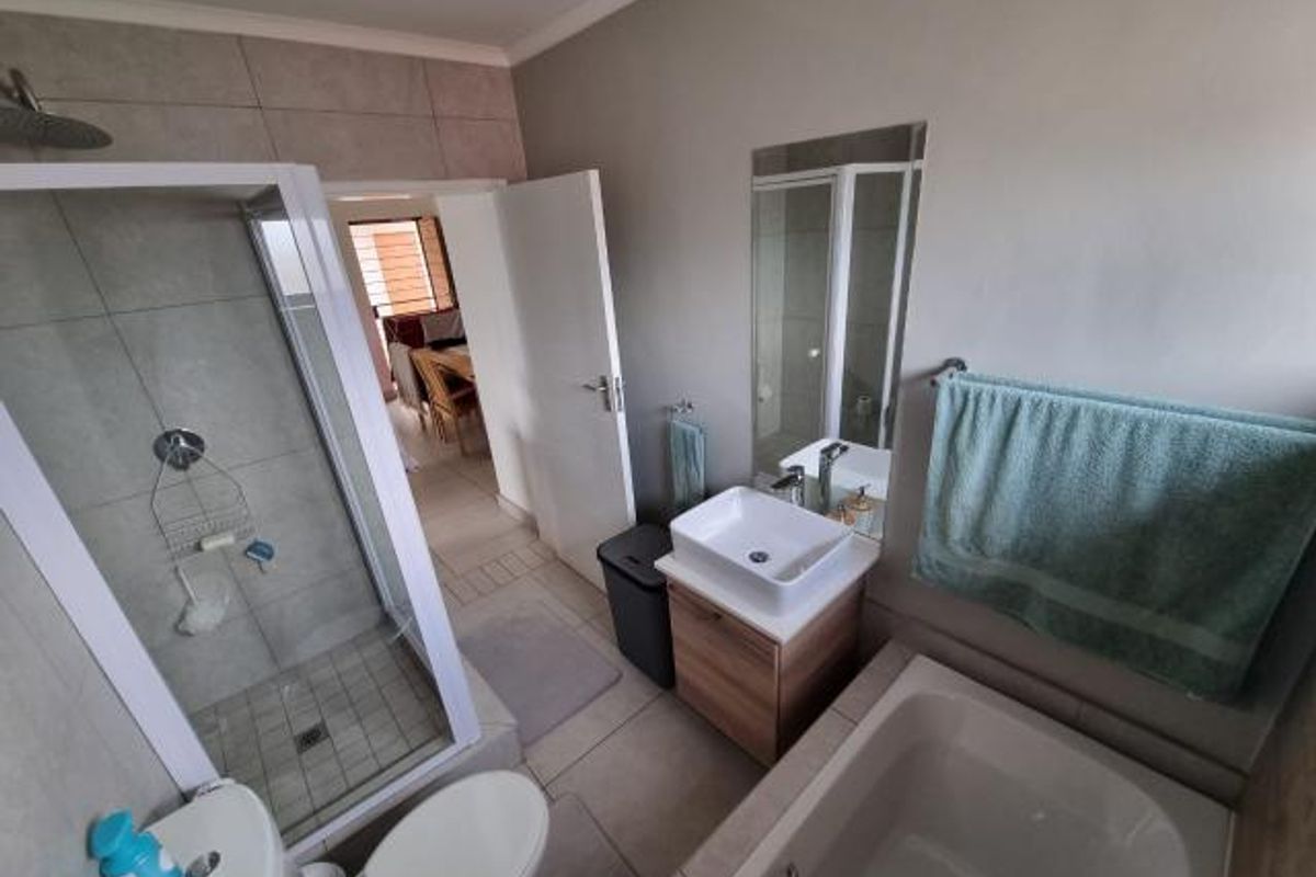 A modern bathroom featuring a glass-enclosed shower, a separate bathtub, a vessel sink vanity, and neutral floor-to-ceiling tiling.
