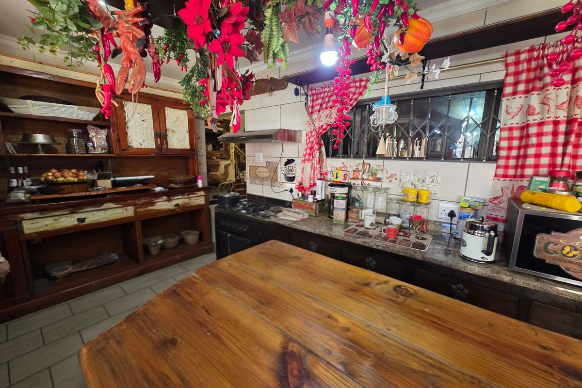 A rustic-style kitchen featuring wooden cabinetry, granite countertops, a built-in hob, and an extractor fan, with tiled flooring and decorative hanging elements.