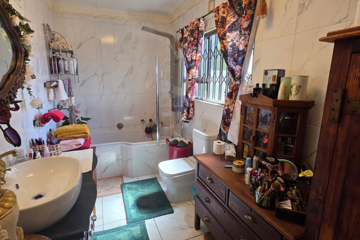 A bathroom featuring marble-look wall and floor tiles, a vessel sink vanity, a bathtub with a shower mixer, and decorative ceiling cornicing.