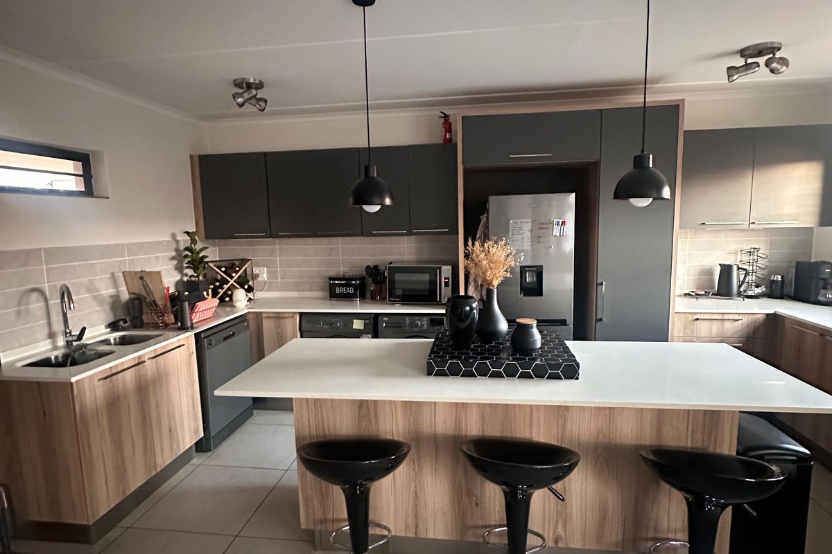 Modern kitchen featuring a central island with breakfast bar seating, ample built-in cabinetry, quartz countertops, and contemporary pendant lighting.