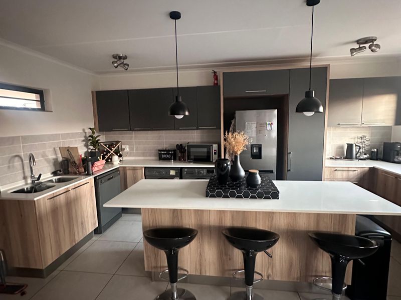 Modern kitchen featuring a central island with breakfast bar seating, ample built-in cabinetry, quartz countertops, and contemporary pendant lighting.
