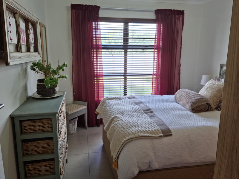 A cozy bedroom featuring tiled flooring and a window with fitted blinds and curtains, providing a functional and comfortable living space.