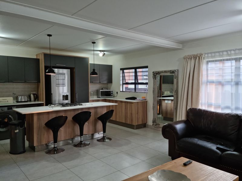 Modern open-plan kitchen and living area featuring a central island, contemporary cabinetry, tiled flooring, and ample natural light through large windows.