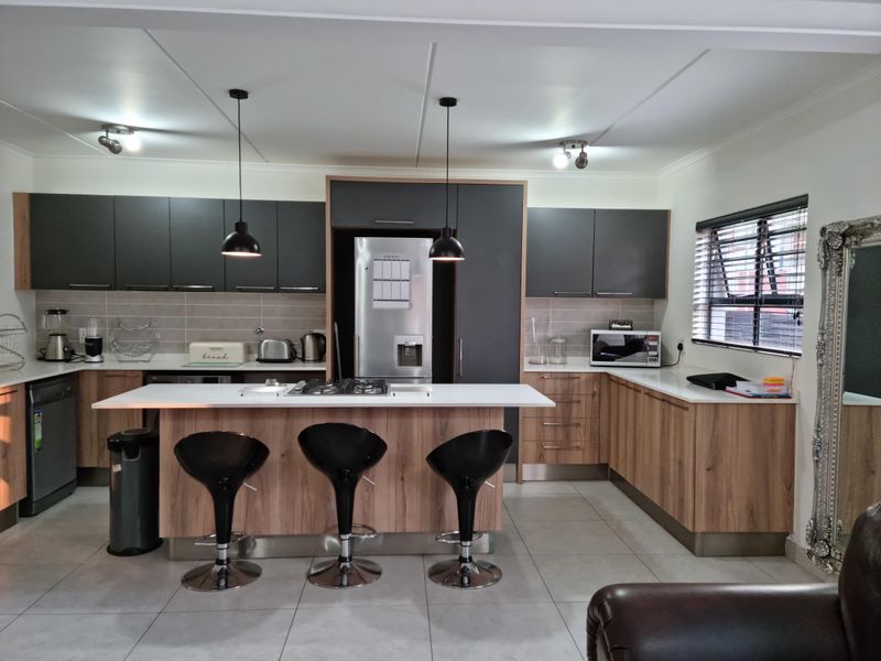 Modern kitchen featuring a central island with gas hob, sleek two-tone cabinetry, tiled flooring, and integrated appliances in a well-lit open-plan layout.