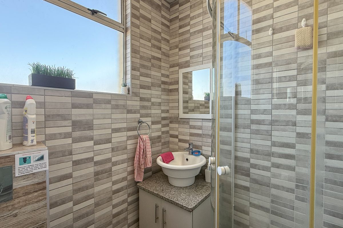 Compact bathroom featuring a modern vessel sink, granite vanity top, glass-enclosed shower, and floor-to-ceiling neutral-toned wall tiling.