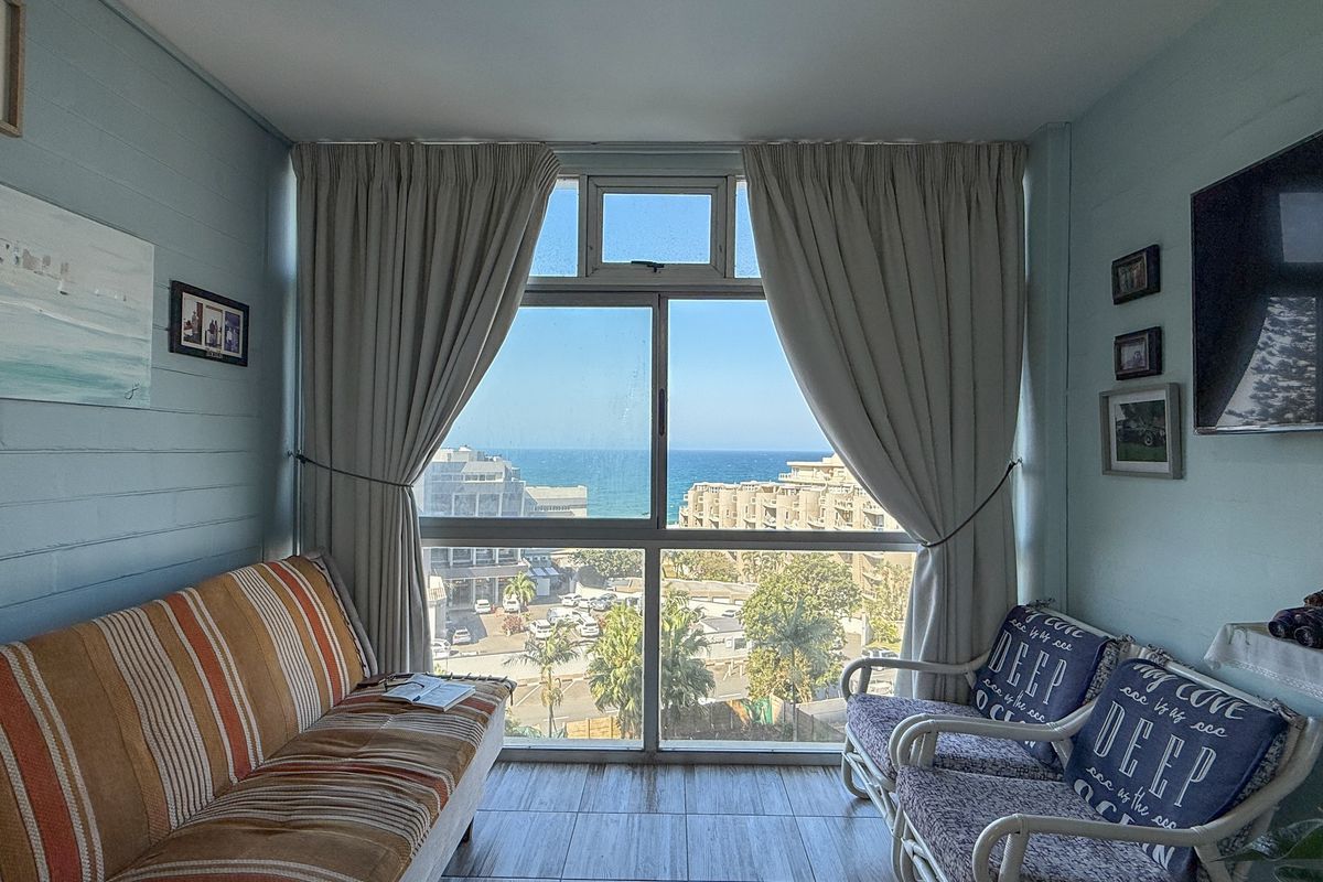 A cozy living room featuring large windows that frame a scenic coastal view, providing natural light and an outlook over the surrounding area.