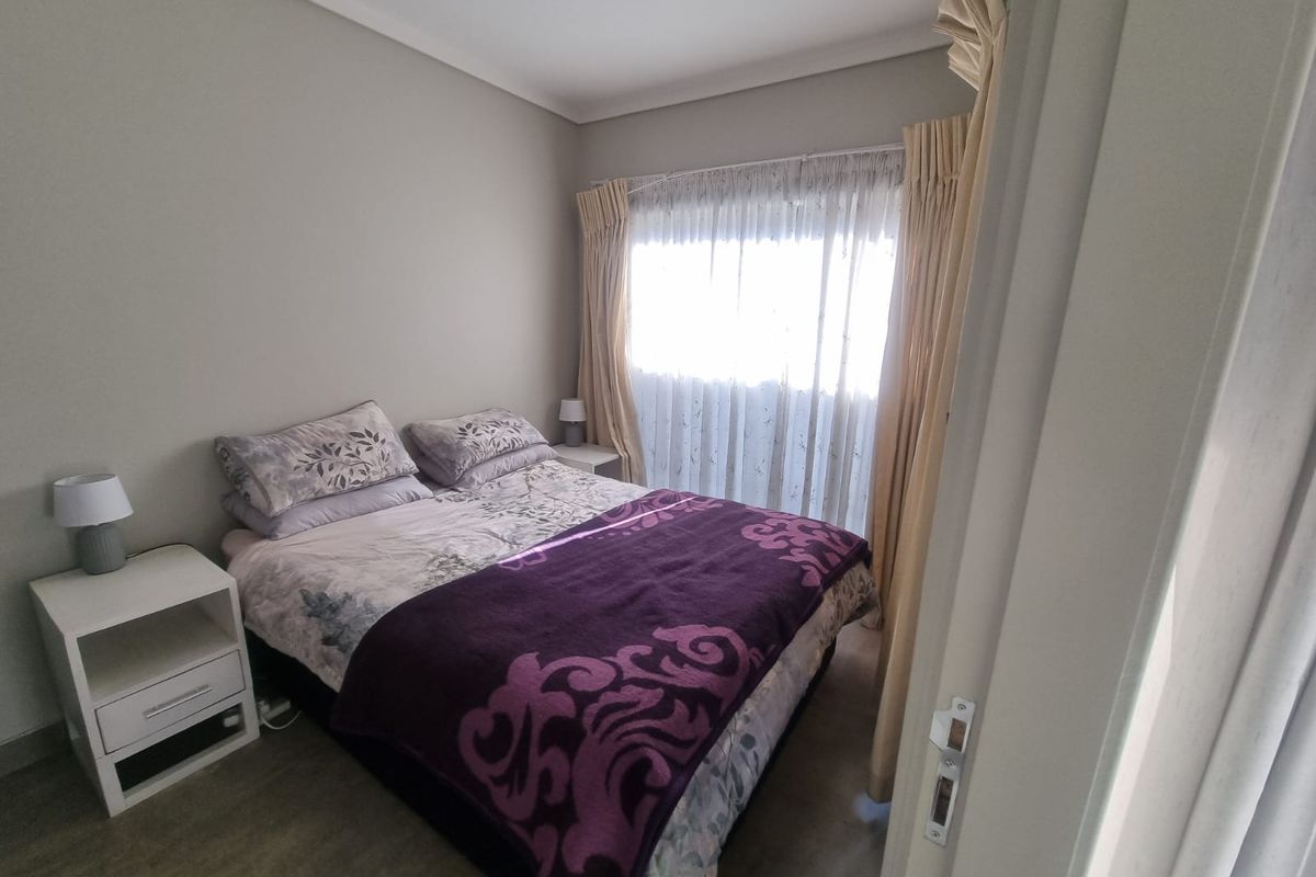 A cozy bedroom featuring neutral wall tones, carpeted flooring, and a window dressed with layered curtains.