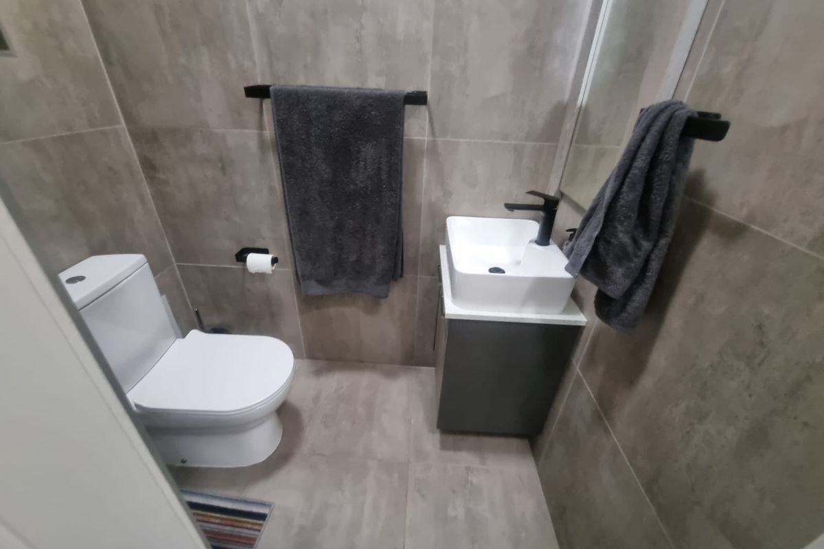 A modern compact bathroom featuring floor-to-ceiling neutral tiling, a contemporary vessel sink with a black faucet, and a wall-mounted toilet.