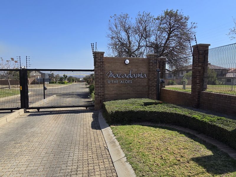 Secure gated entrance to Macadamia at The Aloes, featuring brick perimeter walls, electric fencing, and paved driveway access.