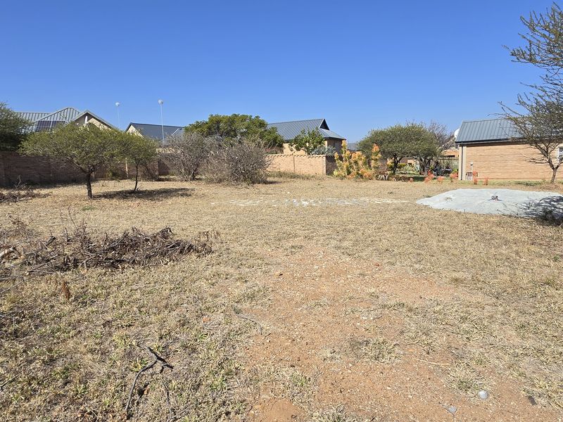 A vacant residential plot featuring established perimeter walls, mature trees, and a level building area ready for development.