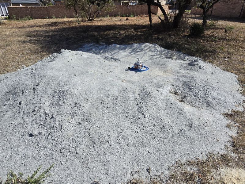 A vacant residential plot featuring a large pile of construction aggregate and exposed ground, suitable for future landscaping or development.