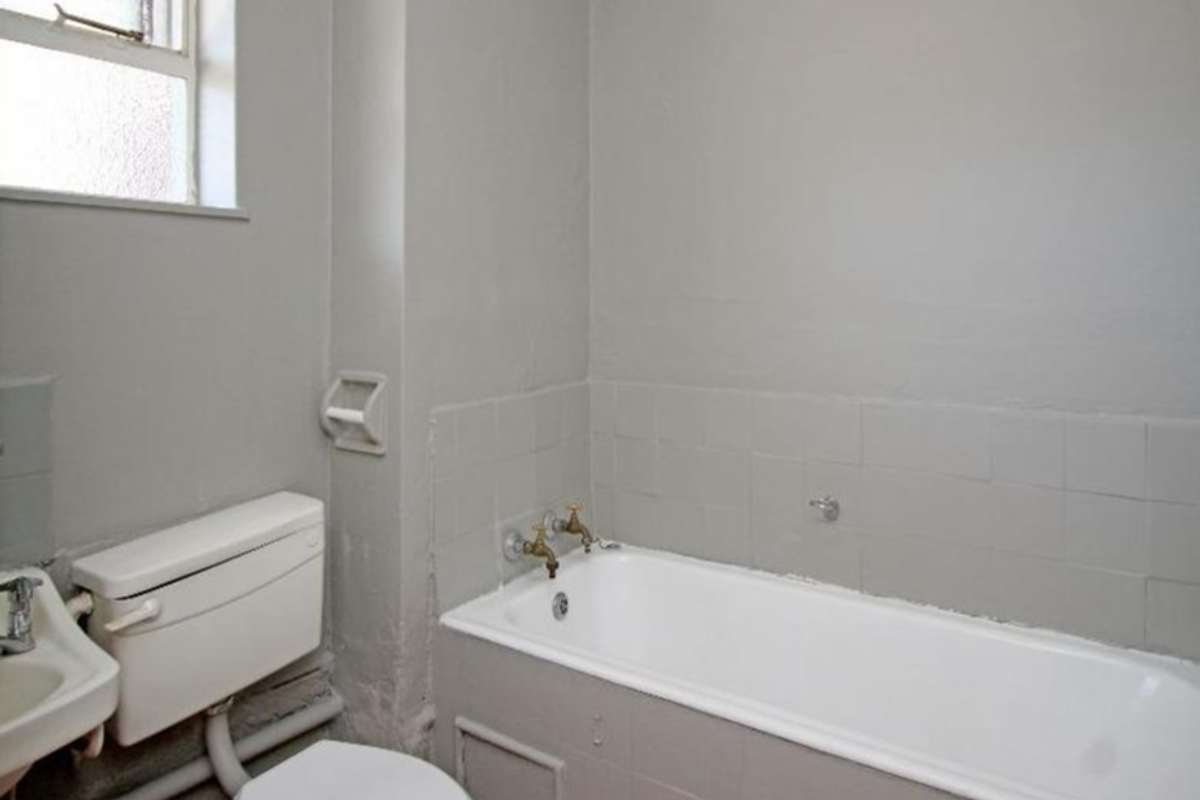 A compact bathroom featuring a standard bathtub, wall-mounted basin, and toilet, with neutral wall finishes and a window for natural light.