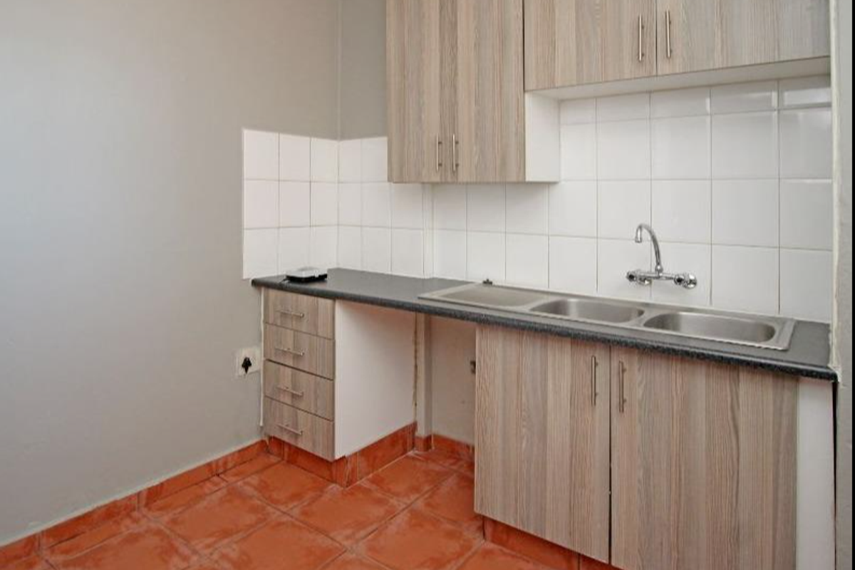 A functional kitchen area featuring wood-look cabinetry, a double stainless steel sink, and tiled splashbacks with terracotta-style floor tiles.