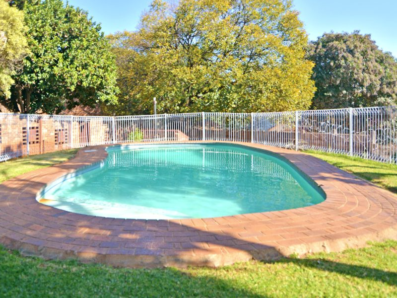 A private swimming pool area featuring brick paving surround and secure perimeter fencing, set within a landscaped garden environment.