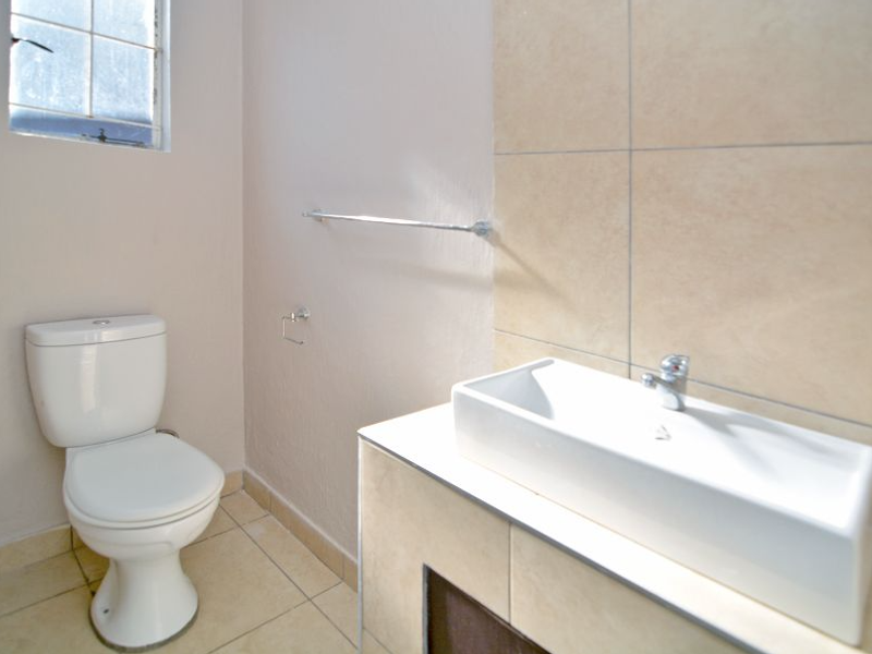 A functional bathroom featuring a modern rectangular vessel sink on a tiled vanity, a standard toilet, and neutral wall tiling.