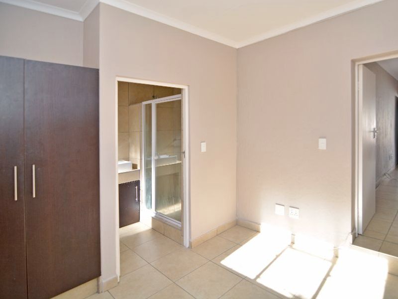 A bedroom featuring tiled flooring, built-in cupboards, and an en-suite bathroom with a glass-enclosed shower.