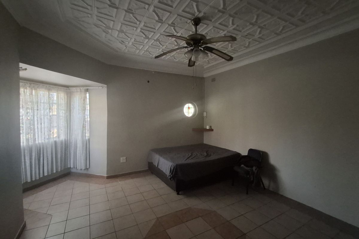 Spacious bedroom featuring a decorative coffered ceiling, ceiling fan, tiled flooring, and a unique circular accent window.