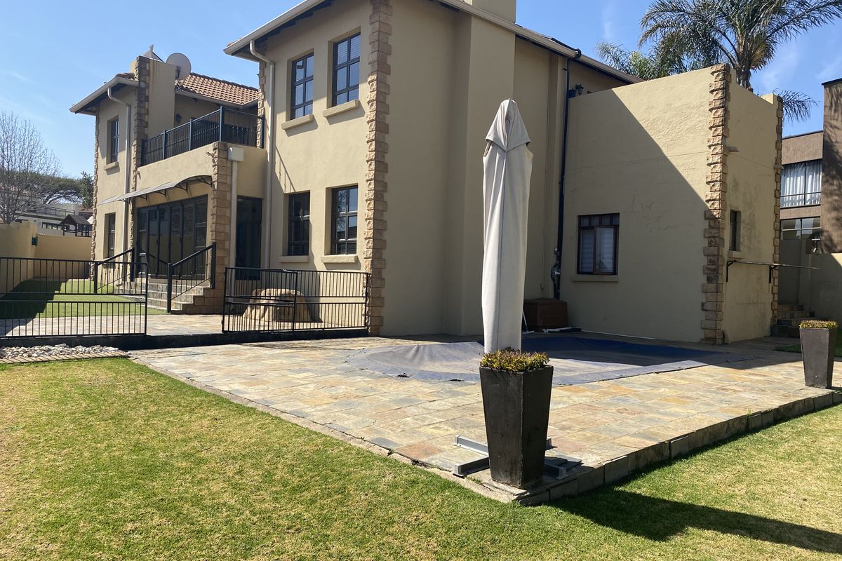 Rear view of the property featuring a stone-paved patio, swimming pool, and a landscaped garden with a balcony overlooking the outdoor area.