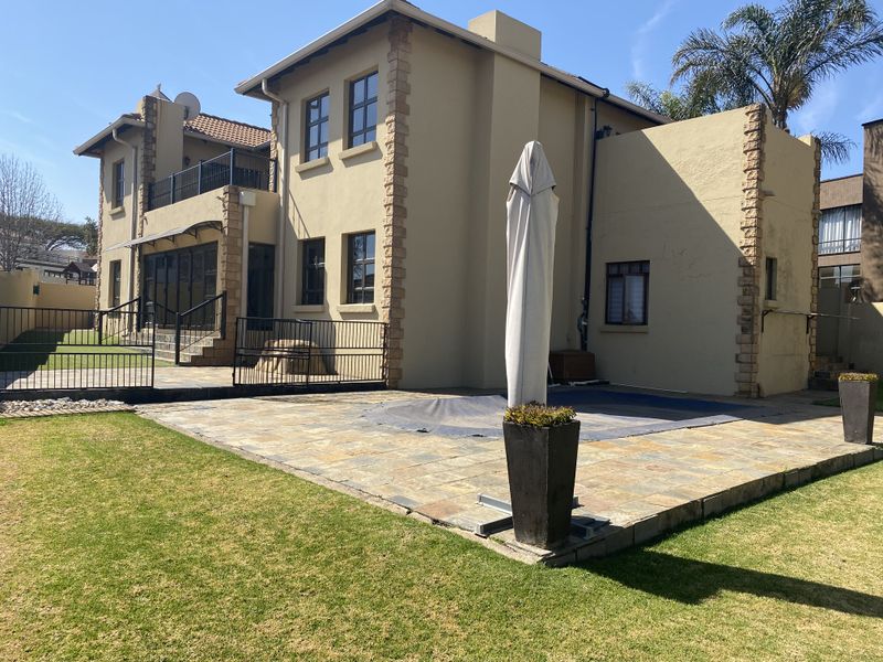 Rear view of the property featuring a stone-paved patio, swimming pool, and a landscaped garden with a balcony overlooking the outdoor area.