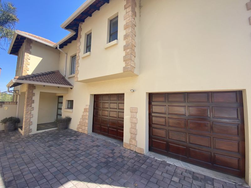 Front elevation of a double-story house featuring a paved driveway, double wooden garage doors, and stone-clad architectural detailing.