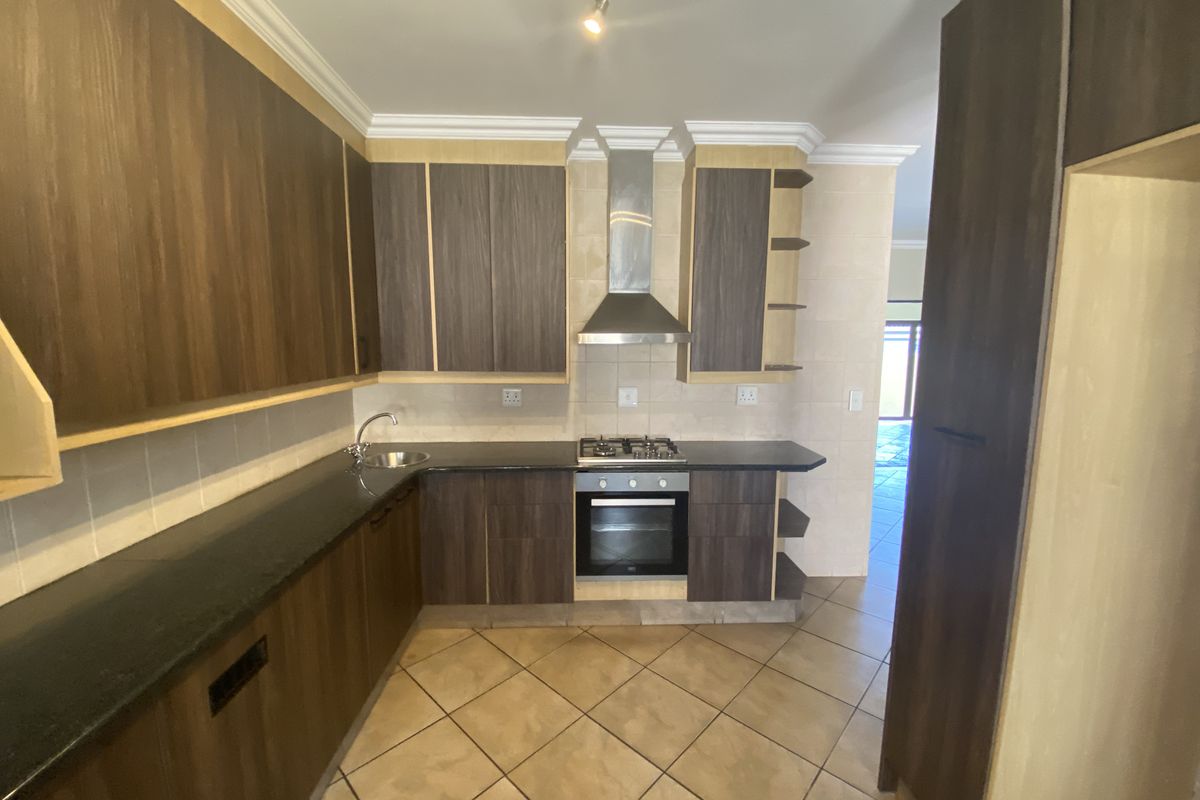 A functional kitchen featuring dark wood cabinetry, granite countertops, a gas hob, built-in oven, and tiled flooring.
