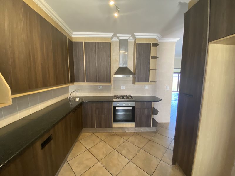 A functional kitchen featuring dark wood cabinetry, granite countertops, a gas hob, built-in oven, and tiled flooring.