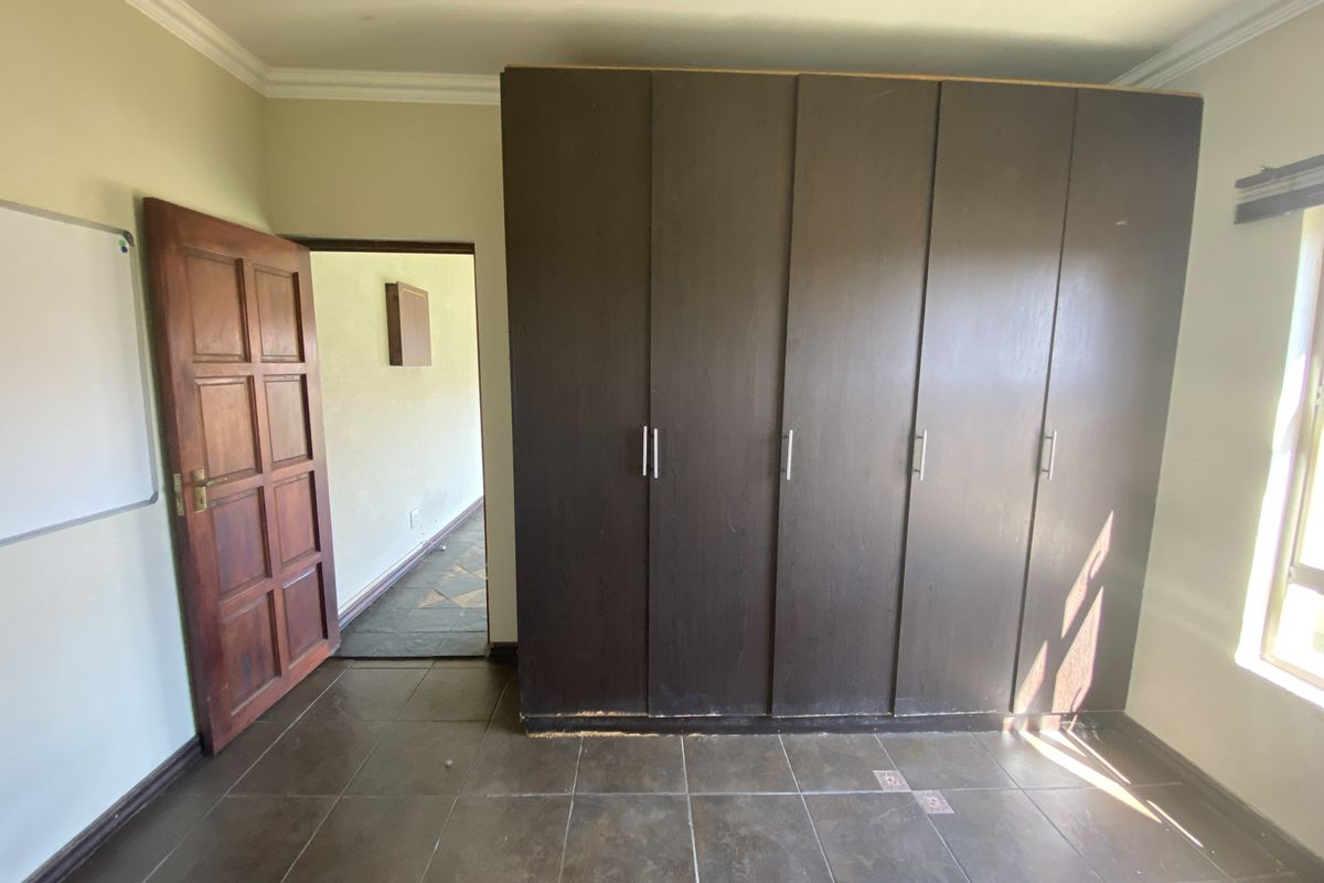 A bedroom featuring dark built-in cupboards, tiled flooring, and a wooden door leading to a hallway.
