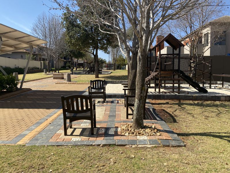 A well-maintained communal garden area featuring paved walkways, mature trees, and a dedicated playground with a sand pit.